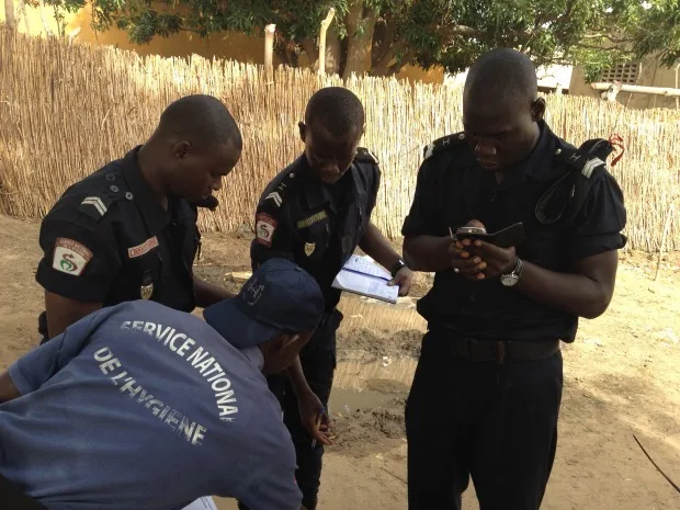 Health agents from the Service National de l'Hygiène gathered around a mobile phone beside a rural water point in Senegal, with paper data sheets in hand
