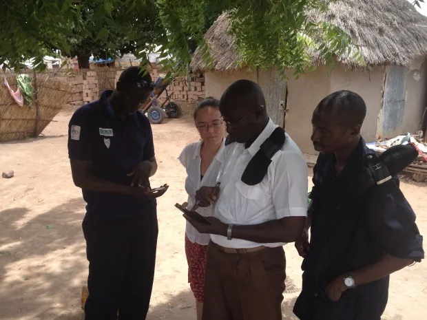 An Aquaya team member accompanying a sampling team in a Senegalese village as two agents enter water sampling data on mobile phones