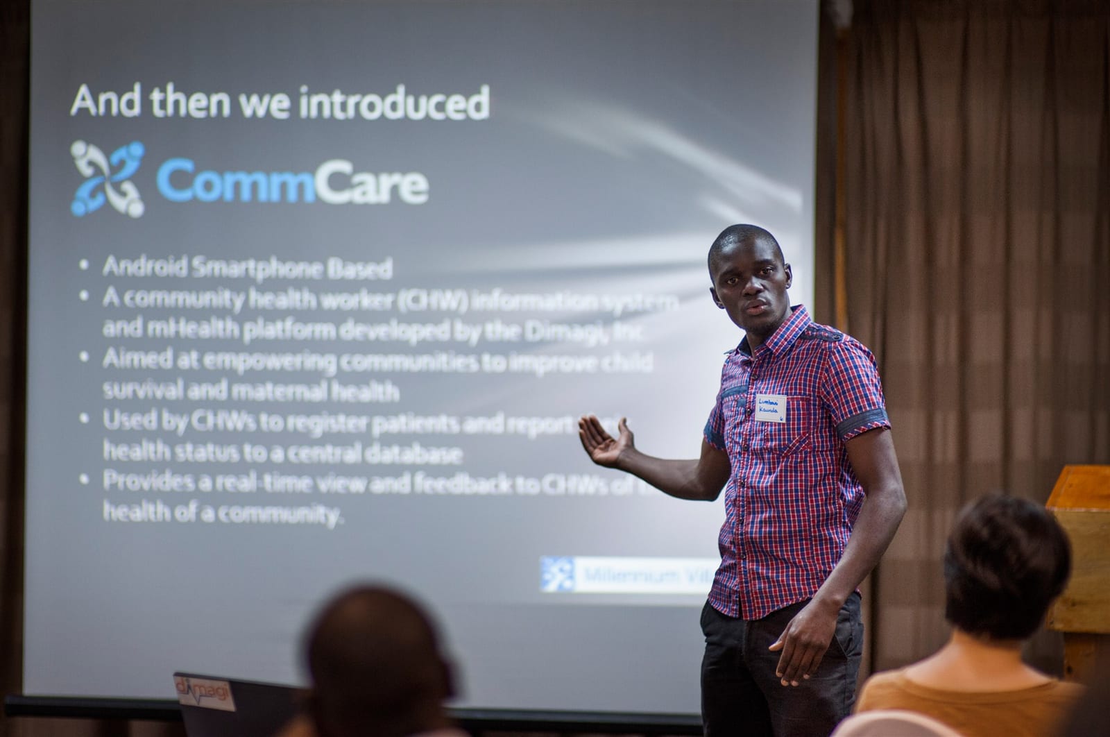 A presenter standing beside a projected slide introducing CommCare as an Android smartphone based information system for community health workers