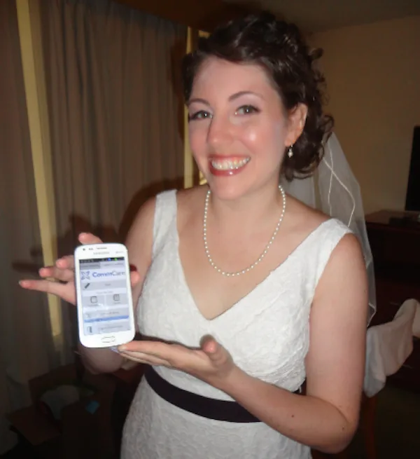 Sarah, in her wedding dress and veil, smiling and holding up a phone running the CommCare wedding app.