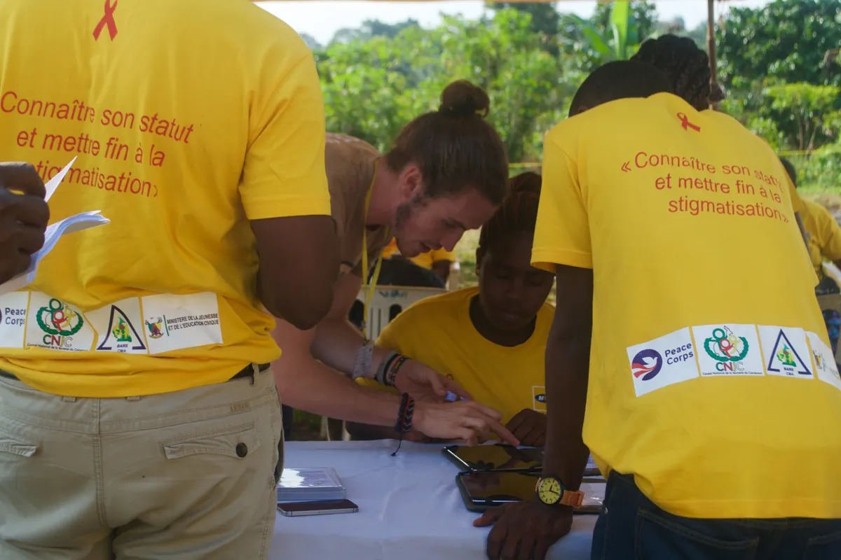 D'Arcy Williams leaning over a table to show two campaign recorders how to use the CommCare app on an Android tablet