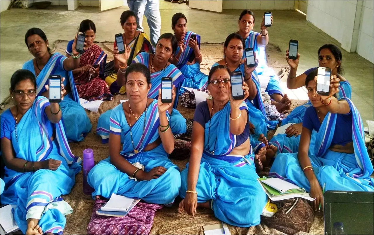 Community health workers seated together, each holding up a mobile phone running a CommCare application